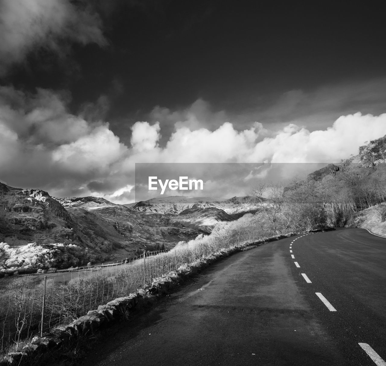 Road passing by mountains against cloudy sky