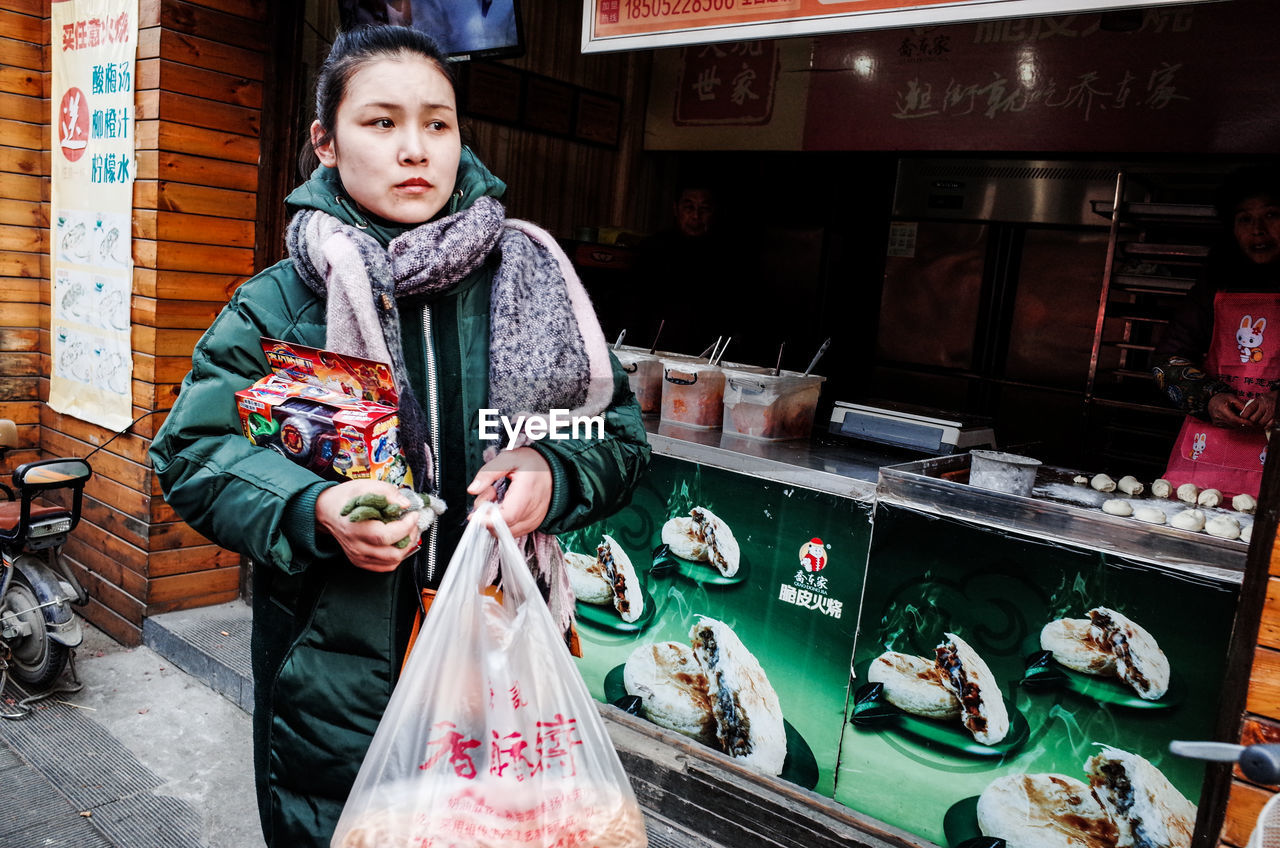 PORTRAIT OF WOMAN STANDING AGAINST STORE