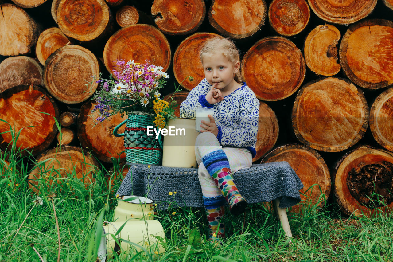 Rustic style, a girl in casual clothes sits on a bench against the background of a woodpile