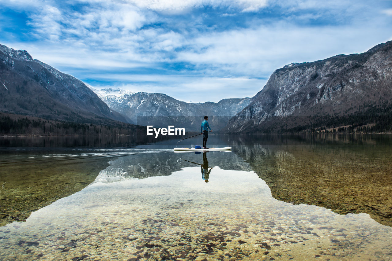 Full length of man paddleboarding in lake against sky