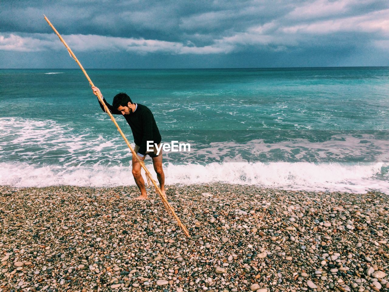 Fisherman with pole on seashore against cloudy sky