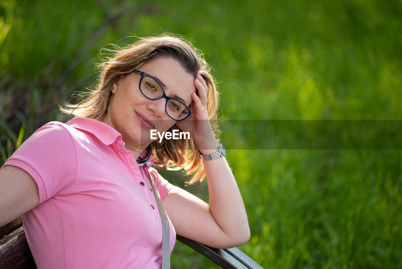 Portrait of smiling woman with head in hand against grassy land