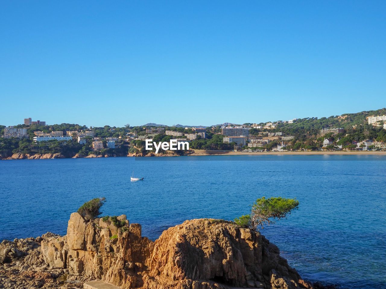 Scenic view of sea by townscape against clear blue sky