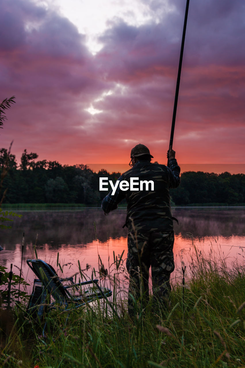 REAR VIEW OF MAN STANDING ON LAKE AGAINST SKY