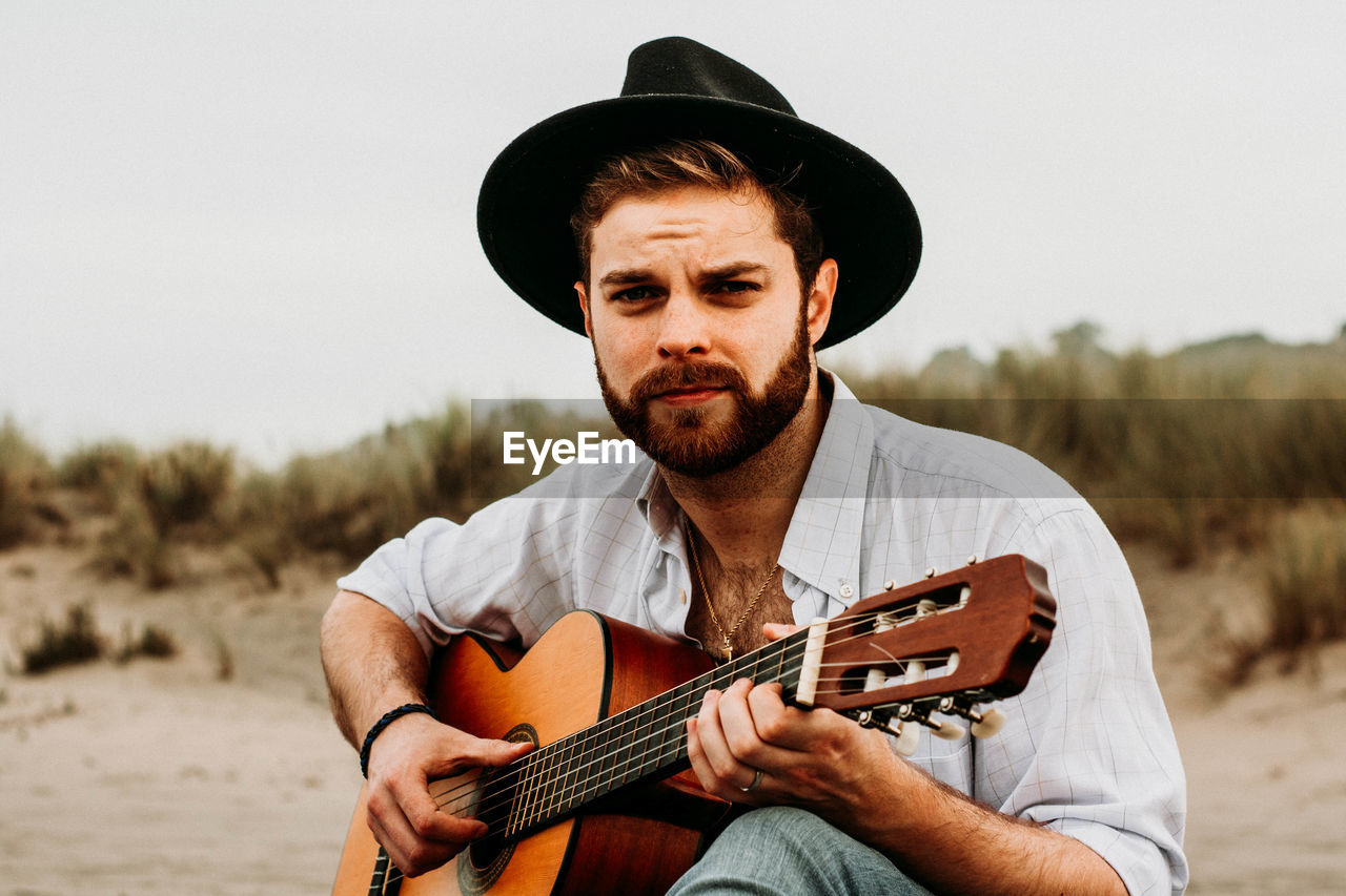 Portrait of young man holding guitar at beach