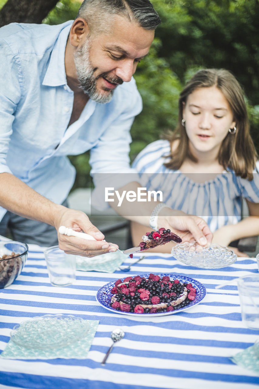 Man serving berry tart to daughter at table in backyard