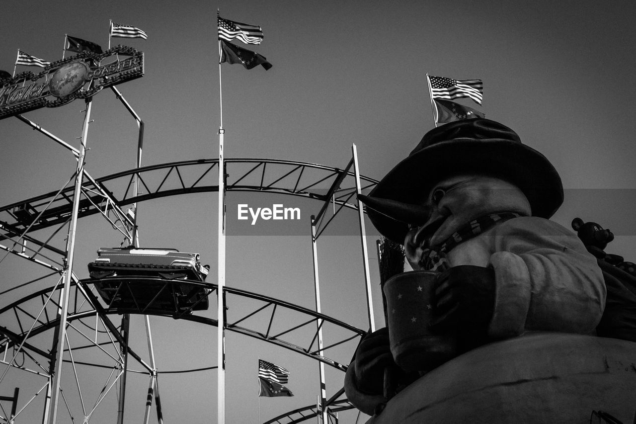 Low angle view of rollercoaster and american flag over statue