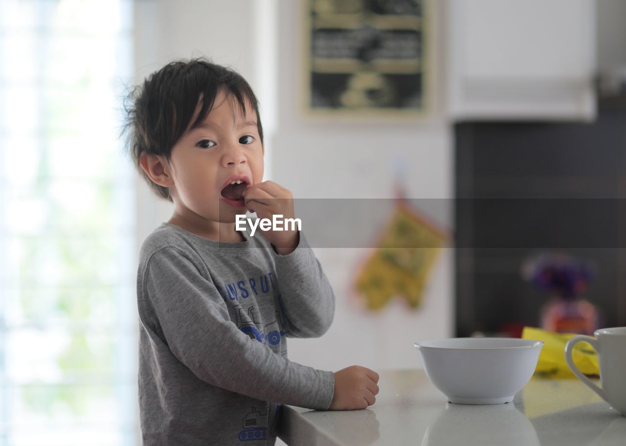 Portrait of boy eating food in kitchen