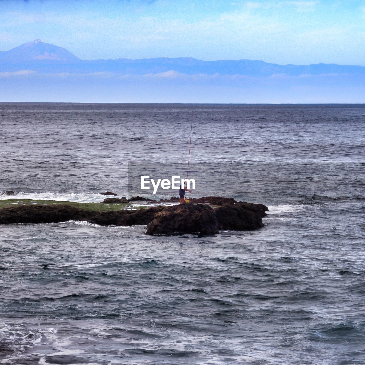 MEN ON ROCK IN SEA AGAINST SKY