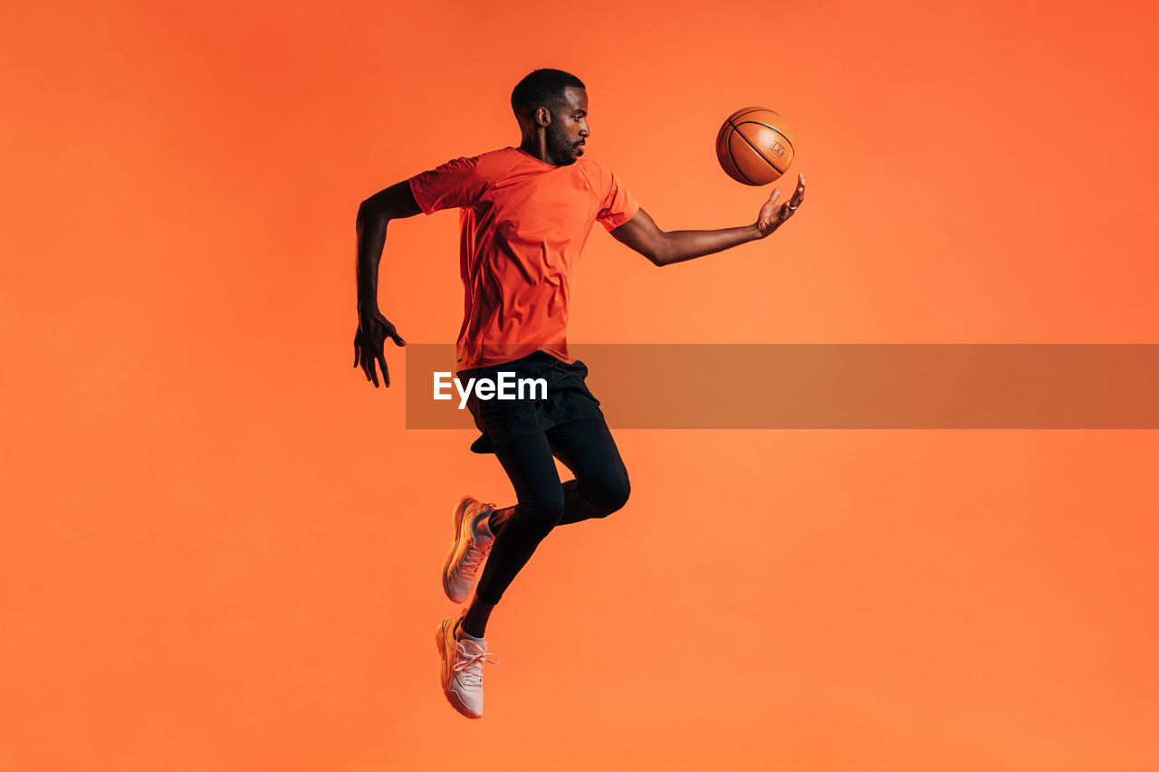 Man with basketball jumping against orange background