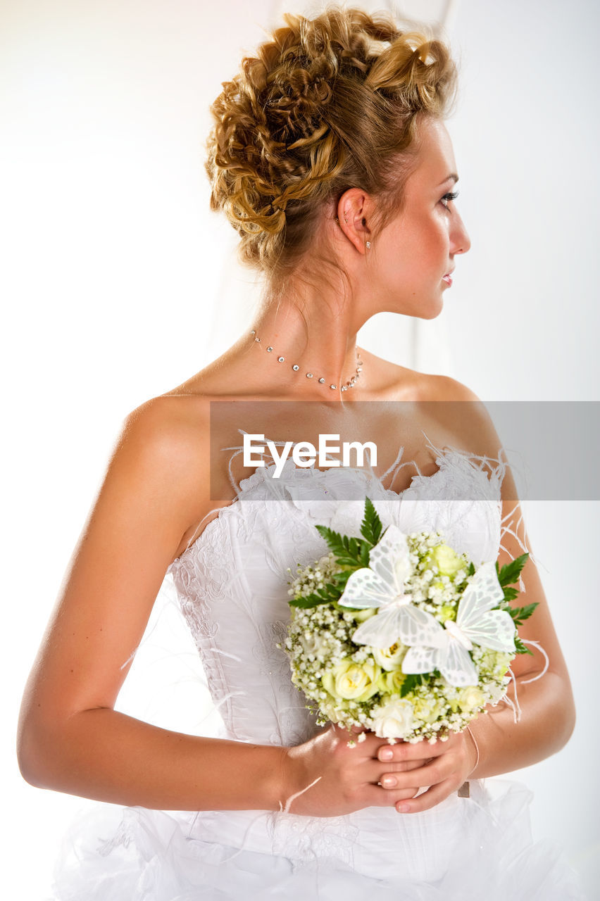 Bride with bouquet looking away while standing against arch