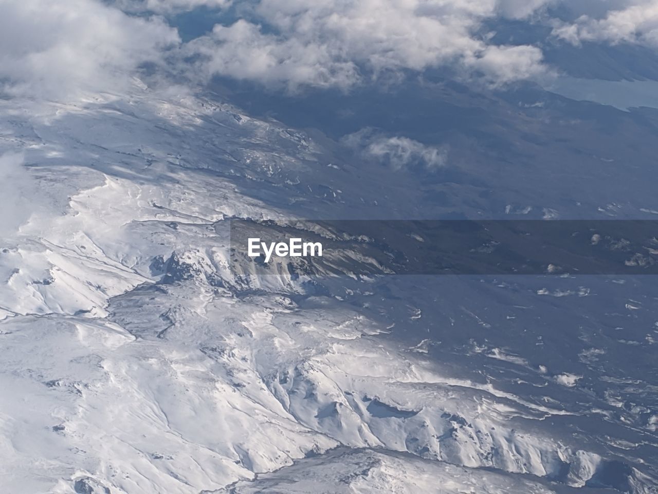 AERIAL VIEW OF SNOWCAPPED MOUNTAIN AGAINST CLOUDY SKY