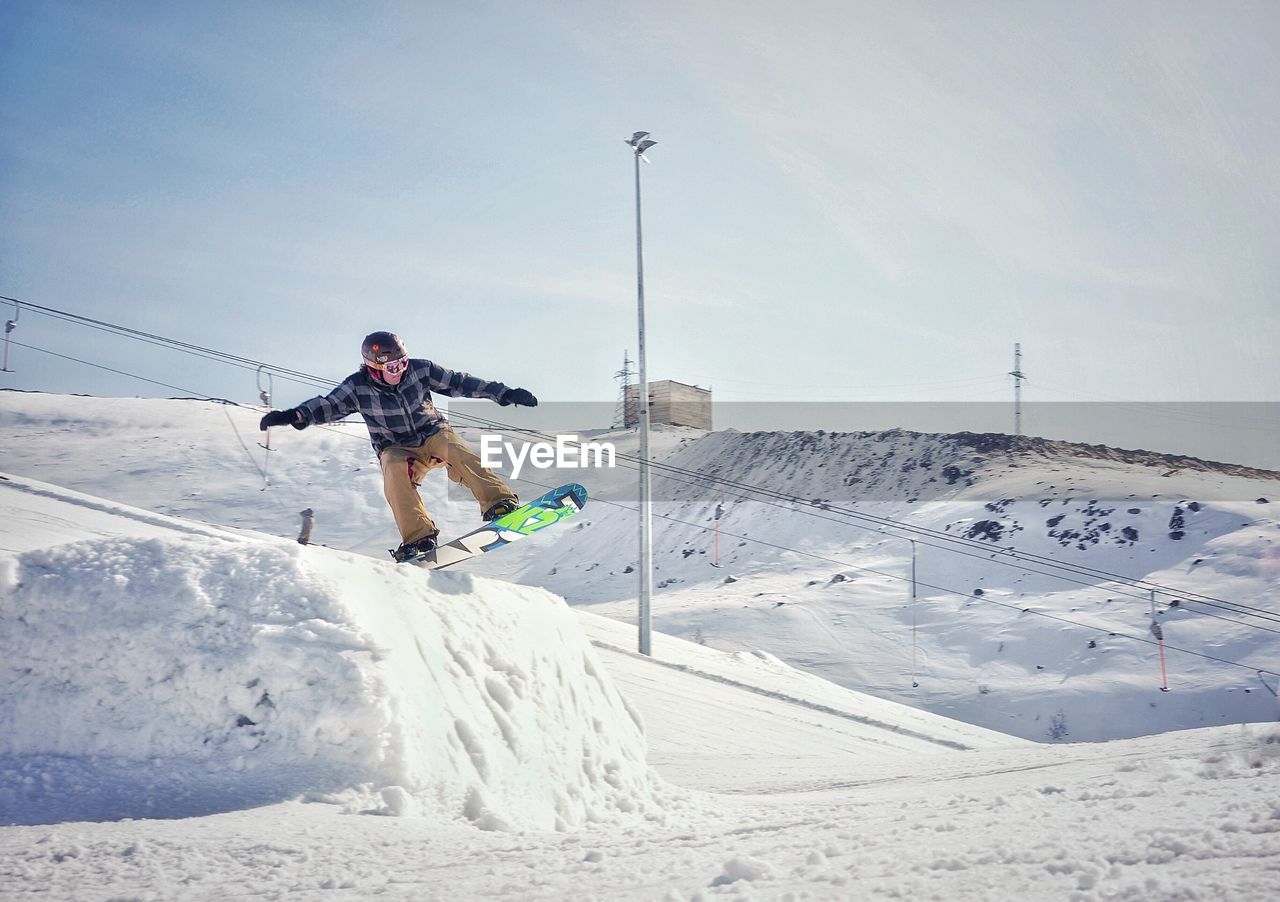 MAN SKATEBOARDING ON SNOW COVERED LANDSCAPE