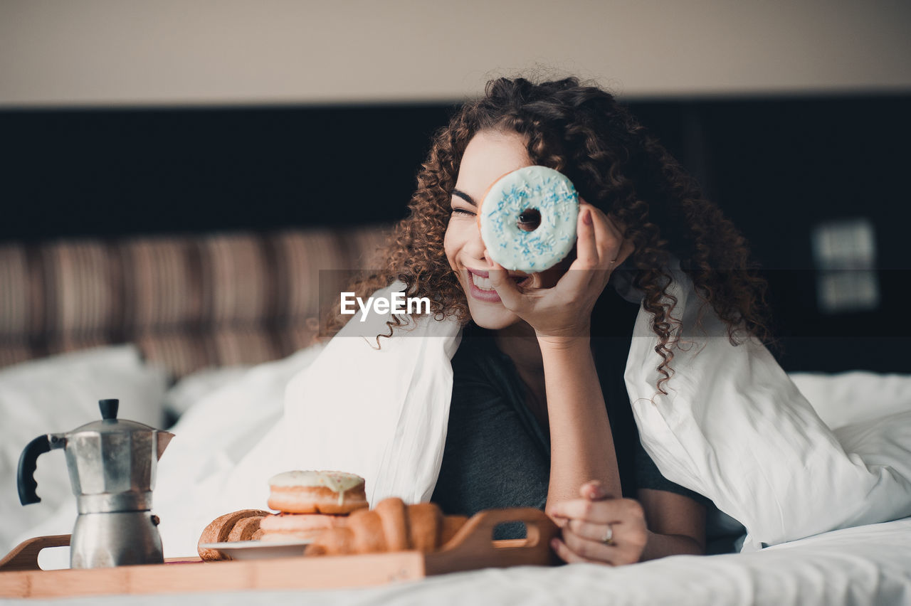 Happy woman looking through doughnut on bed