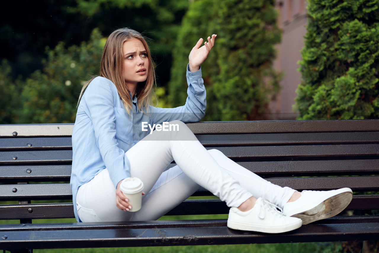 portrait of young woman using mobile phone while sitting on bench