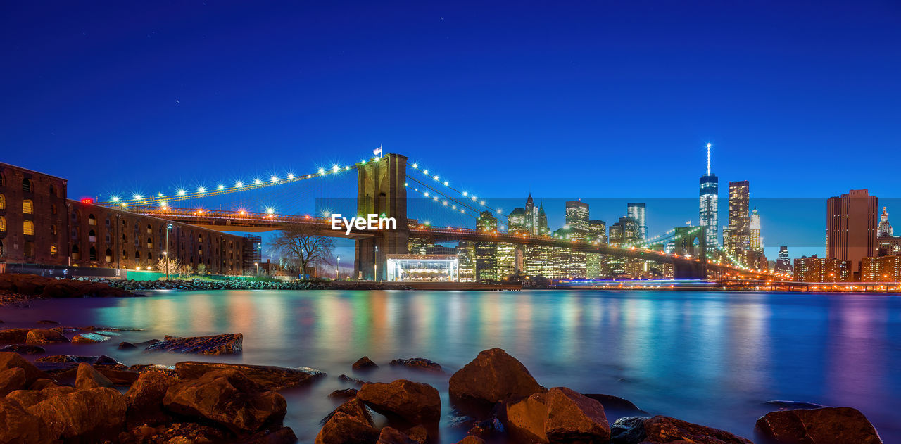 illuminated bridge over river against clear sky at night