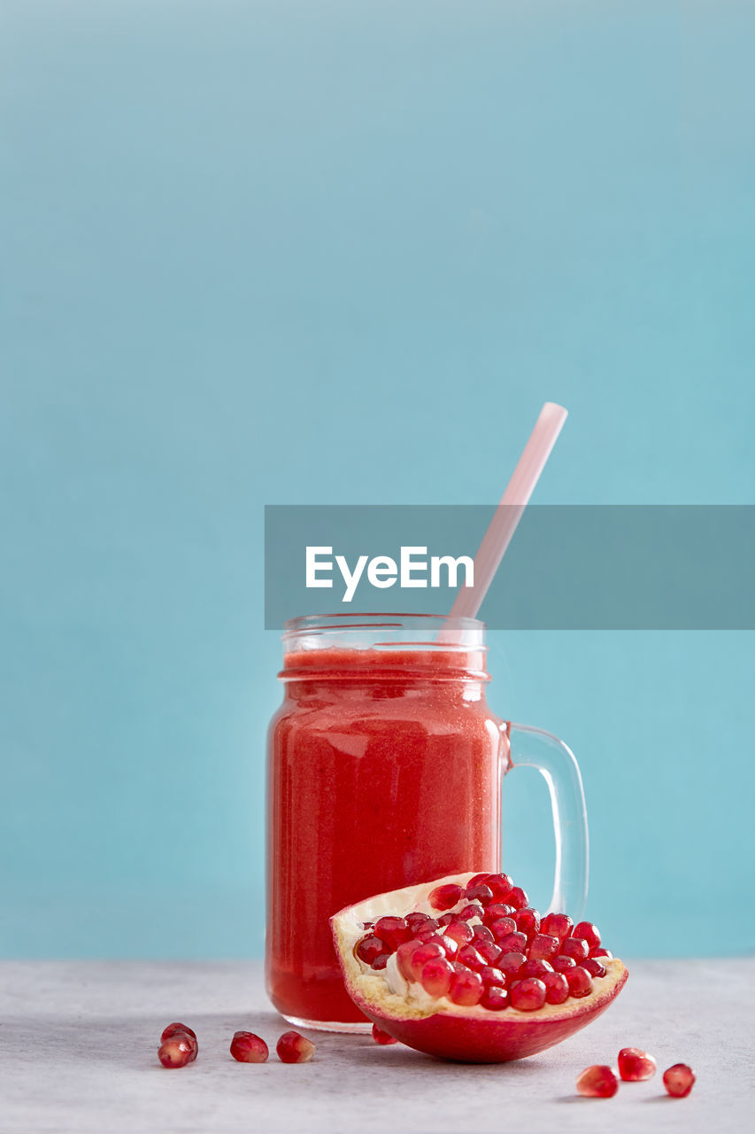 Close-up of red drink in glass with pomegranate on table against blue background