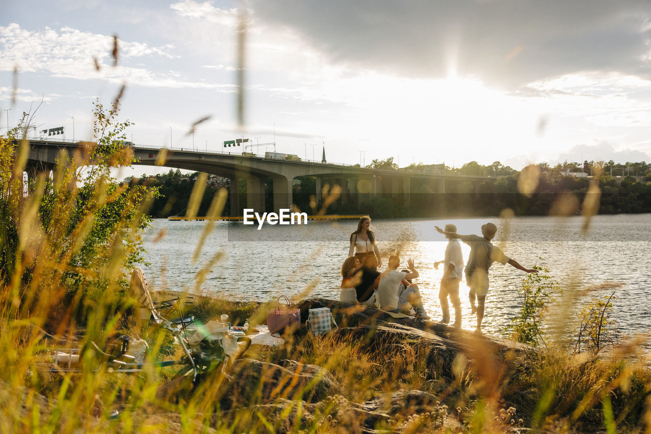 Male and female friends spending leisure time while enjoying picnic near sea at sunset