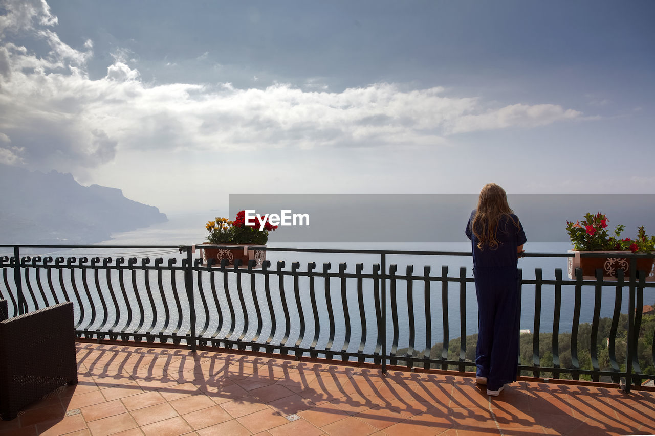 Rear view of woman standing by railing against sea