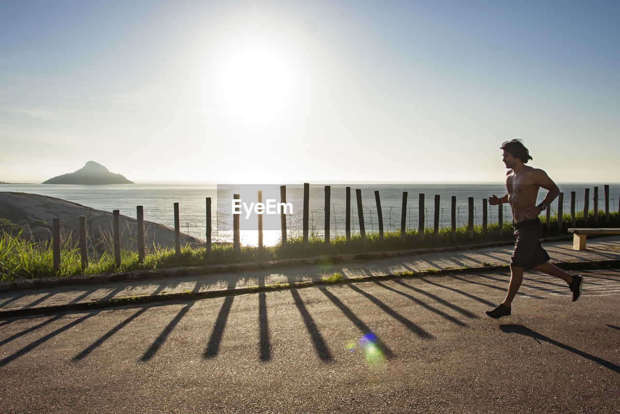 Man running on street by sea against sky during sunny day