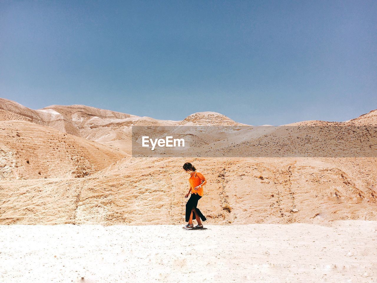 Woman walking against mountains at desert during sunny day