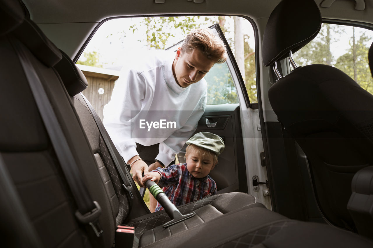 Man with toddler son vacuum cleaning car