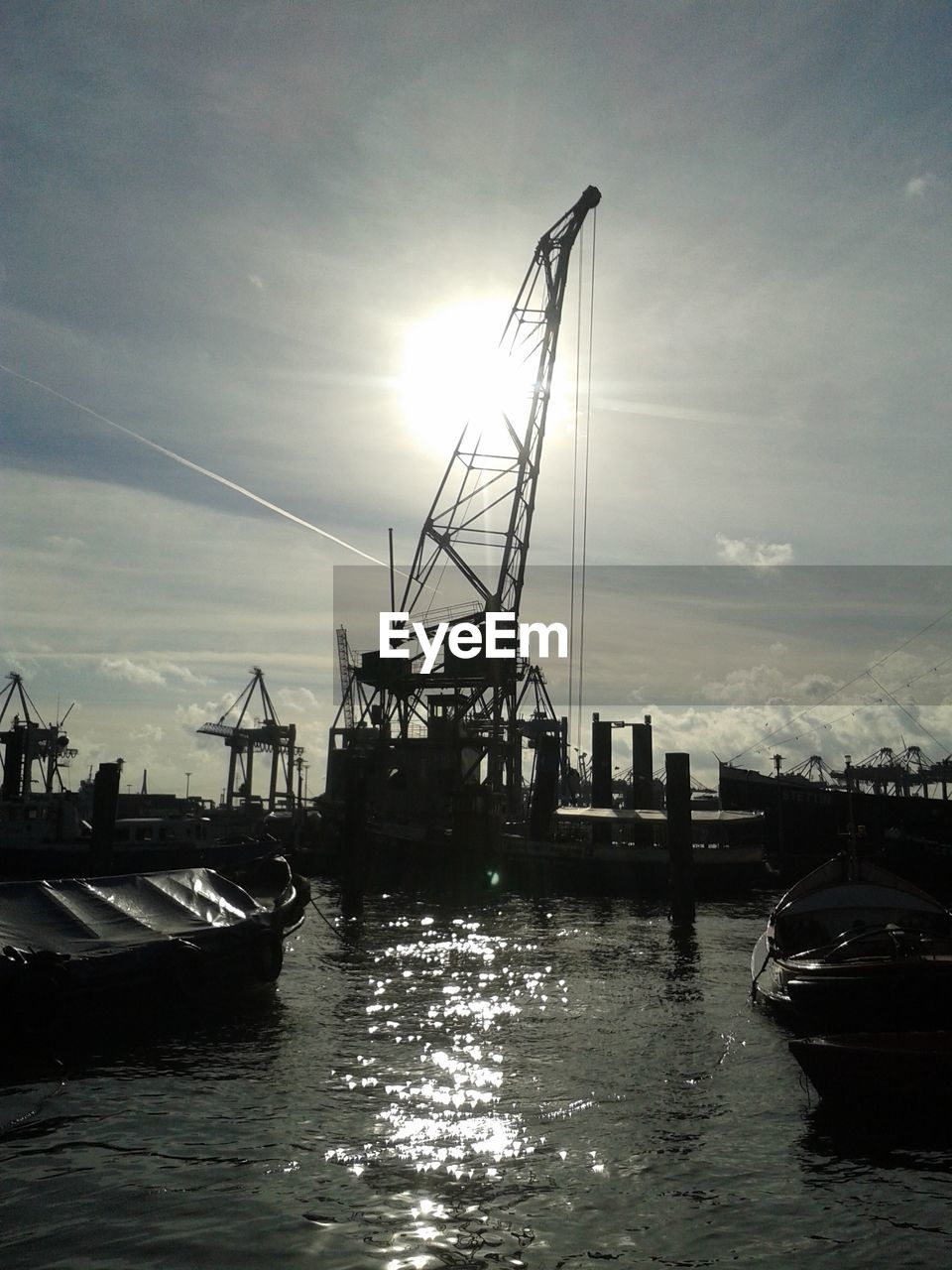 Crane at commercial dock against bright sky