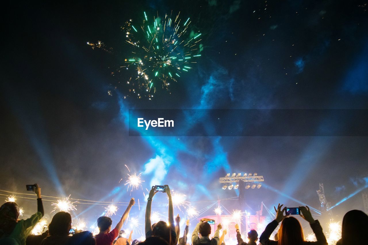 People enjoying concert against firework display at night