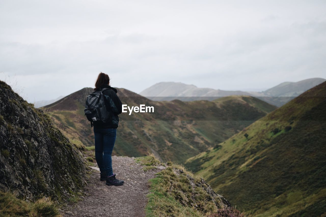 Rear view of hiker standing on trail against sky