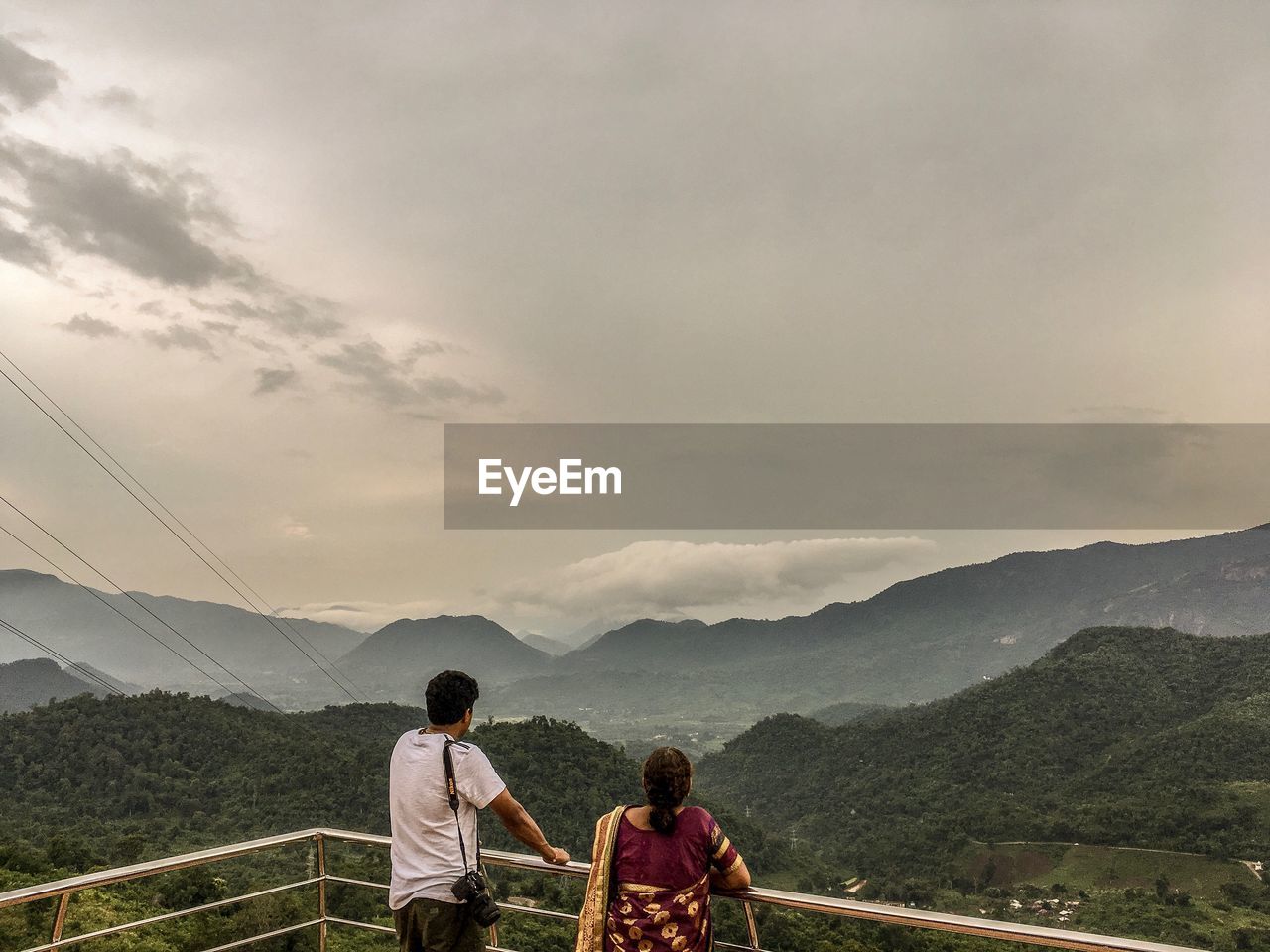 Rear view of mother and son leaning on railing against mountains