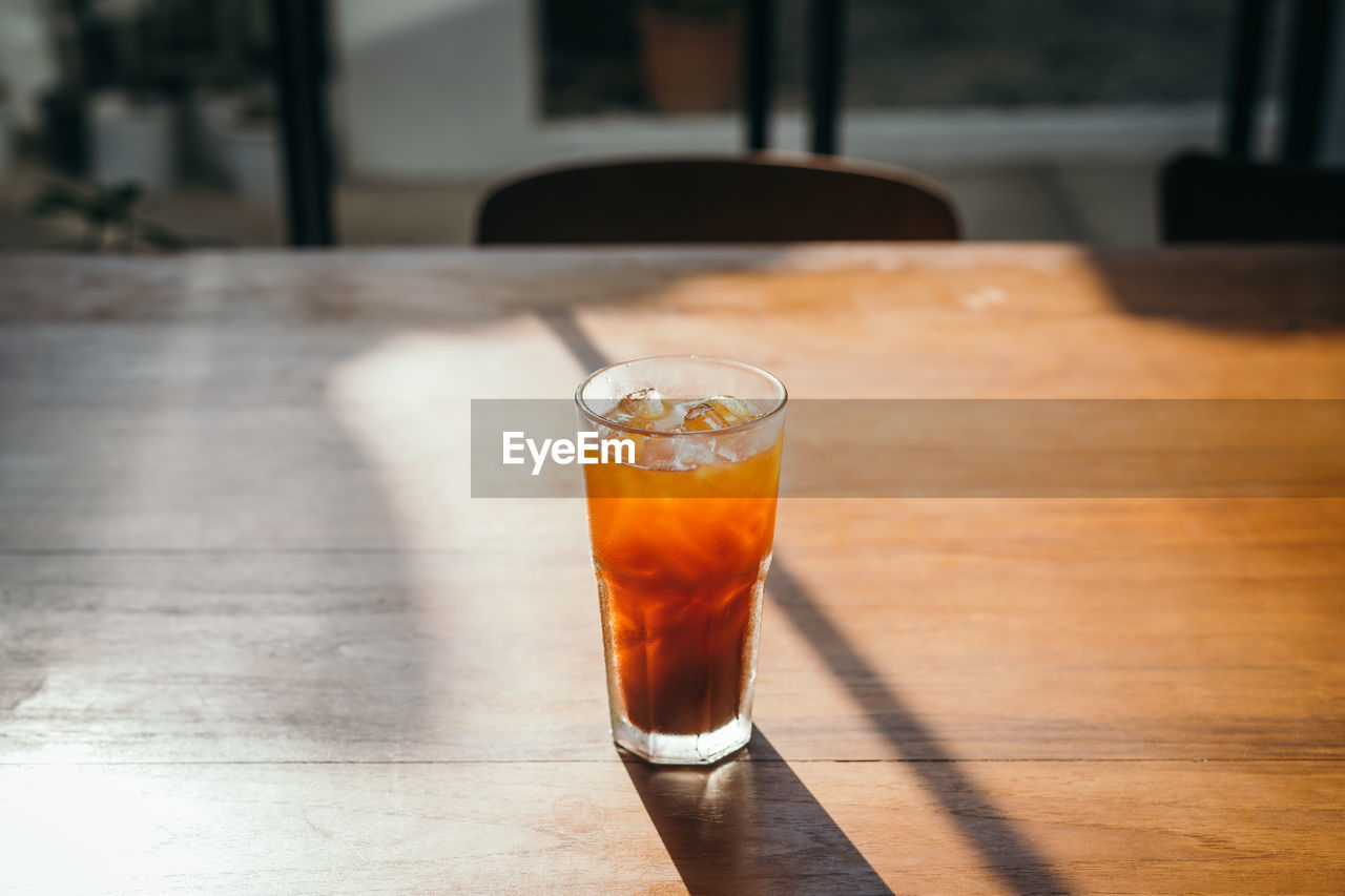 Iced americano coffee on wooden cafe table with sunlight