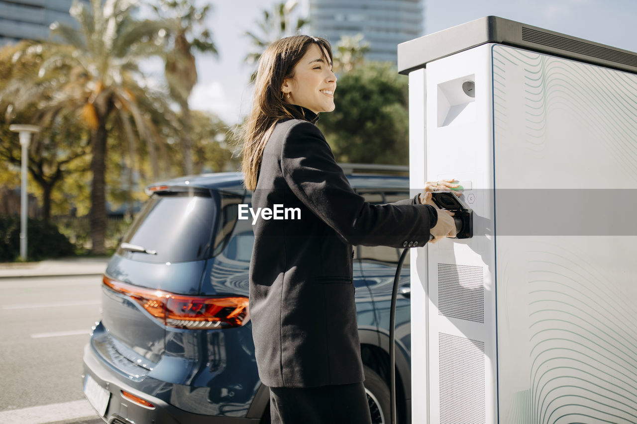 Happy woman charging electric car at charging station