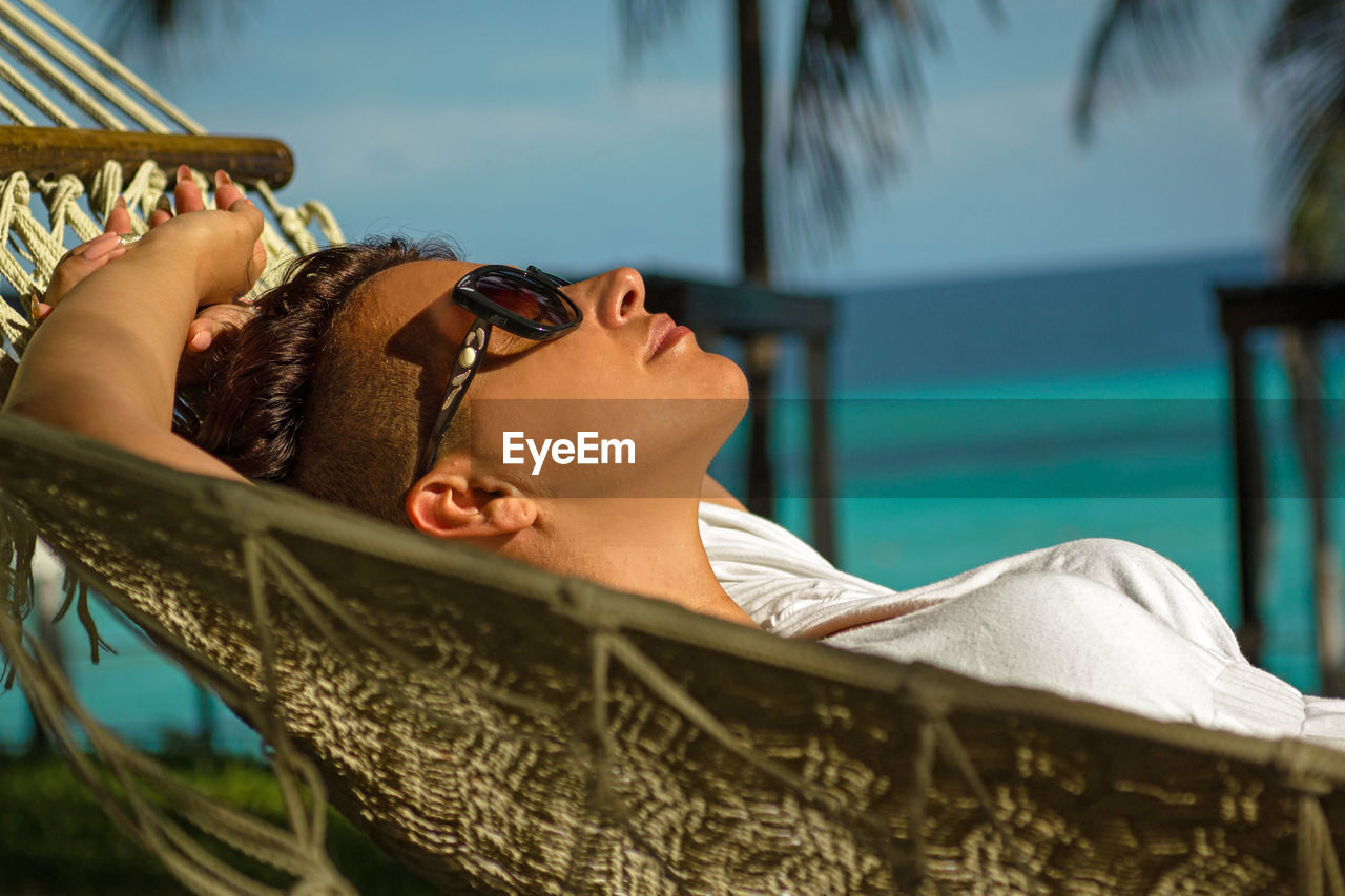 Side view of woman lying in hammock at beach