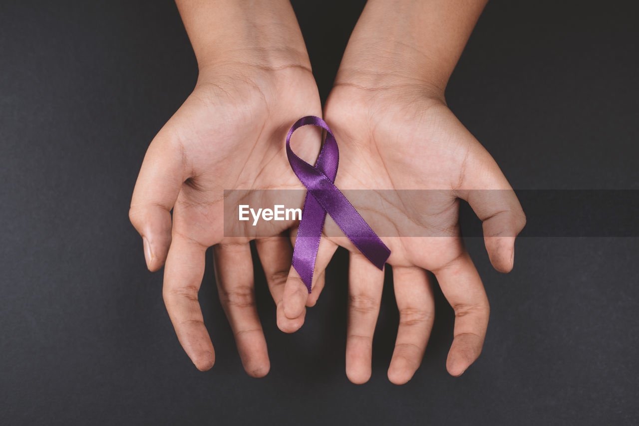 Cropped hands holding ribbon against black background