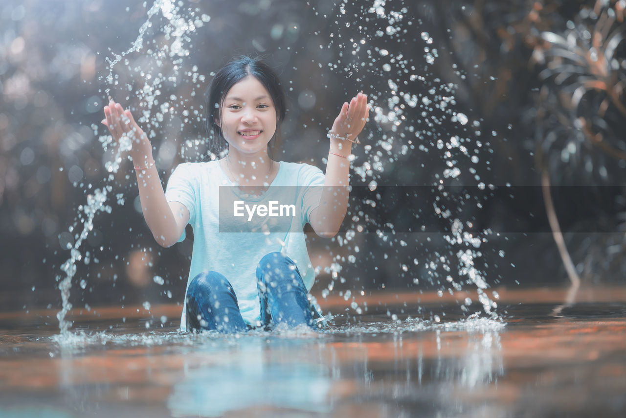 PORTRAIT OF HAPPY GIRL IN WATER AT PARK