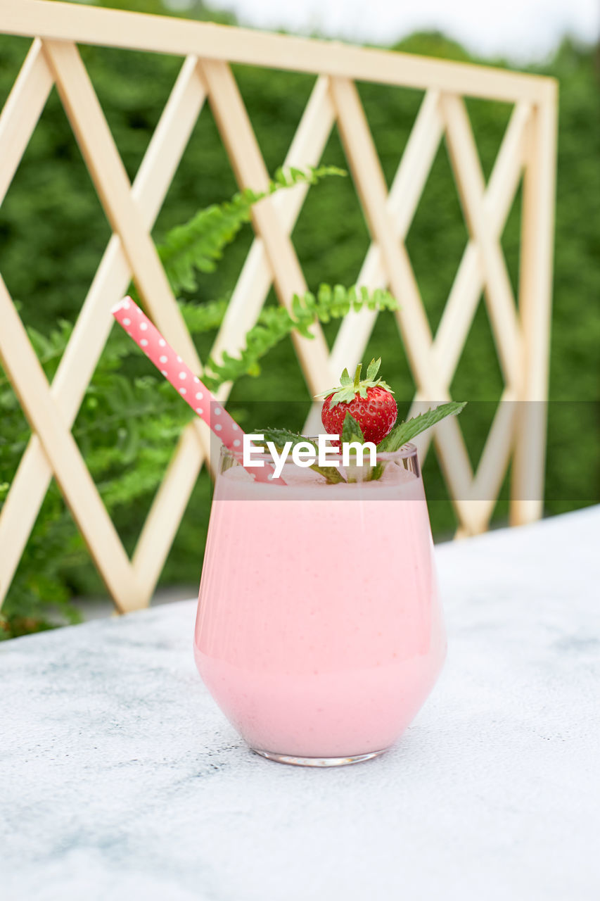 Strawberry smoothie or milkshake with banana and mint in a glass glass on a table in the garden. 