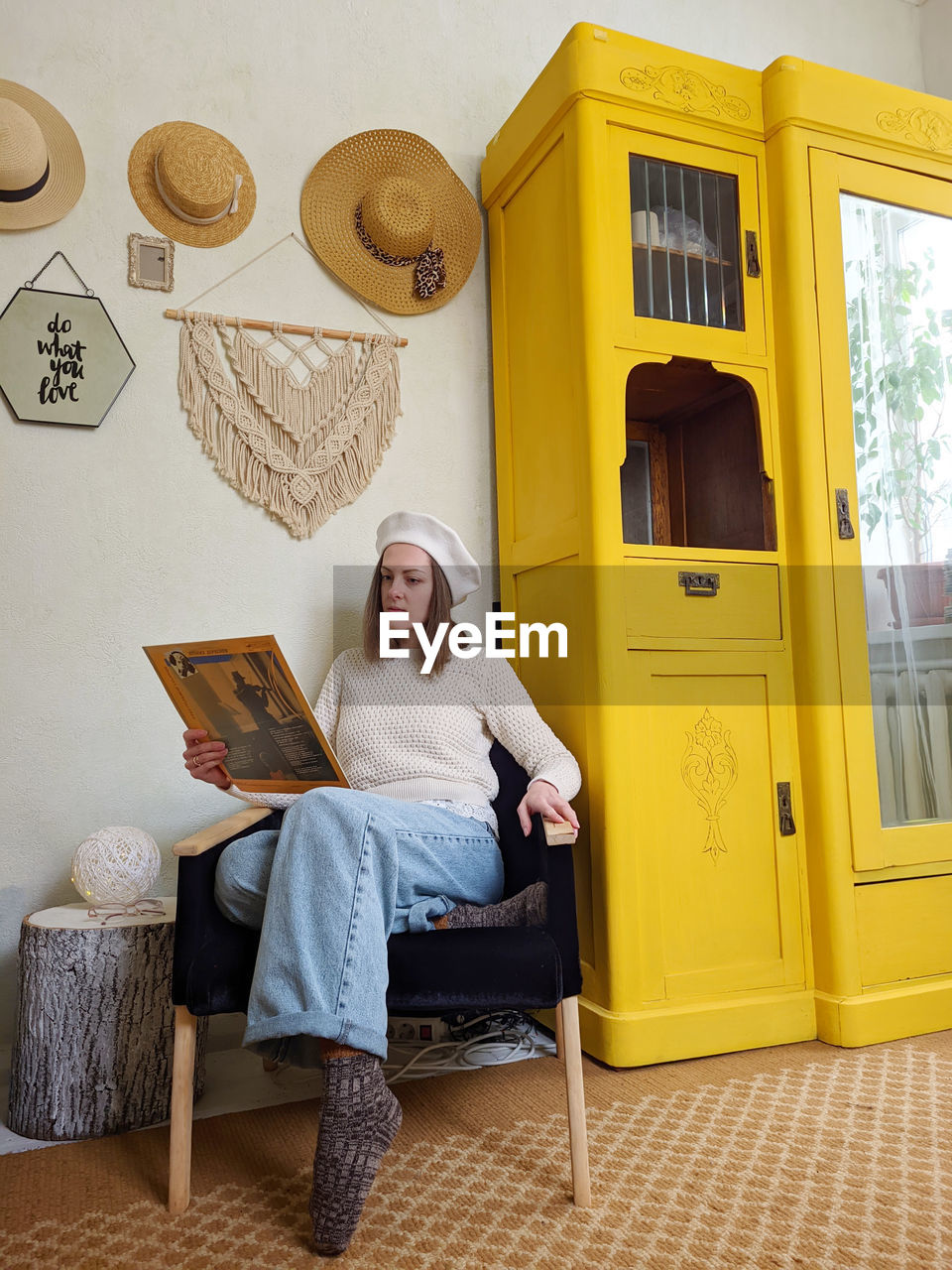 Young woman in beret sits in cozy home, room with music record in hands. vintage yellow cabinet.