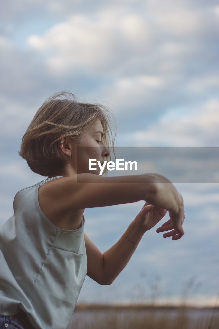 Side view of beautiful woman dancing against cloudy sky