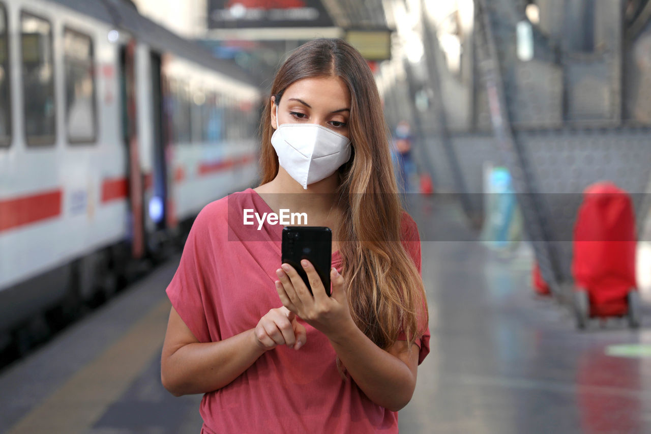 Woman using smartphone while standing at railroad station