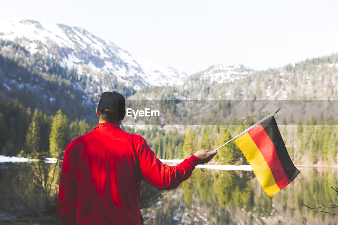 Rear view of man with flags standing against snowcapped mountains