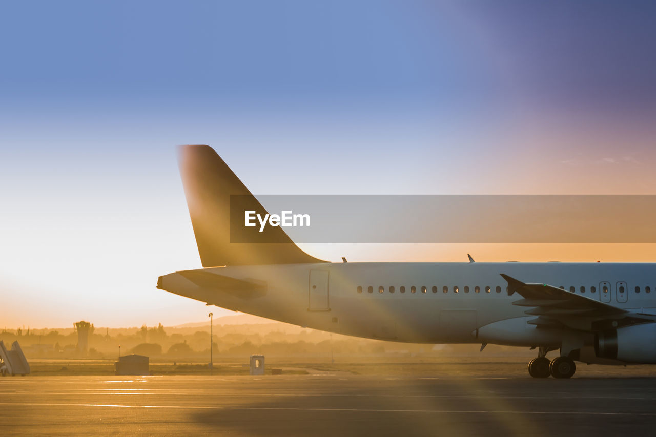 Airplane on airport runway against sky during sunset