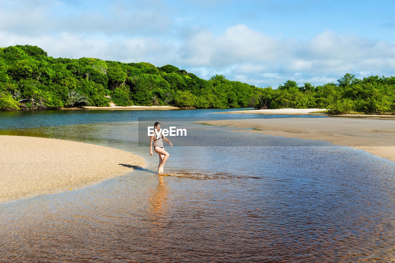 water, shore, land, beach, sky, one person, body of water, nature, sea, vacation, tree, full length, trip, holiday, beauty in nature, cloud, plant, sand, adult, day, leisure activity, scenics - nature, coast, tranquility, lifestyles, travel, outdoors, travel destinations, ocean, tranquil scene, summer, bay, standing, idyllic, walking, tropical climate, women, environment, rear view, landscape, sunlight, young adult, casual clothing, motion, men, relaxation, person