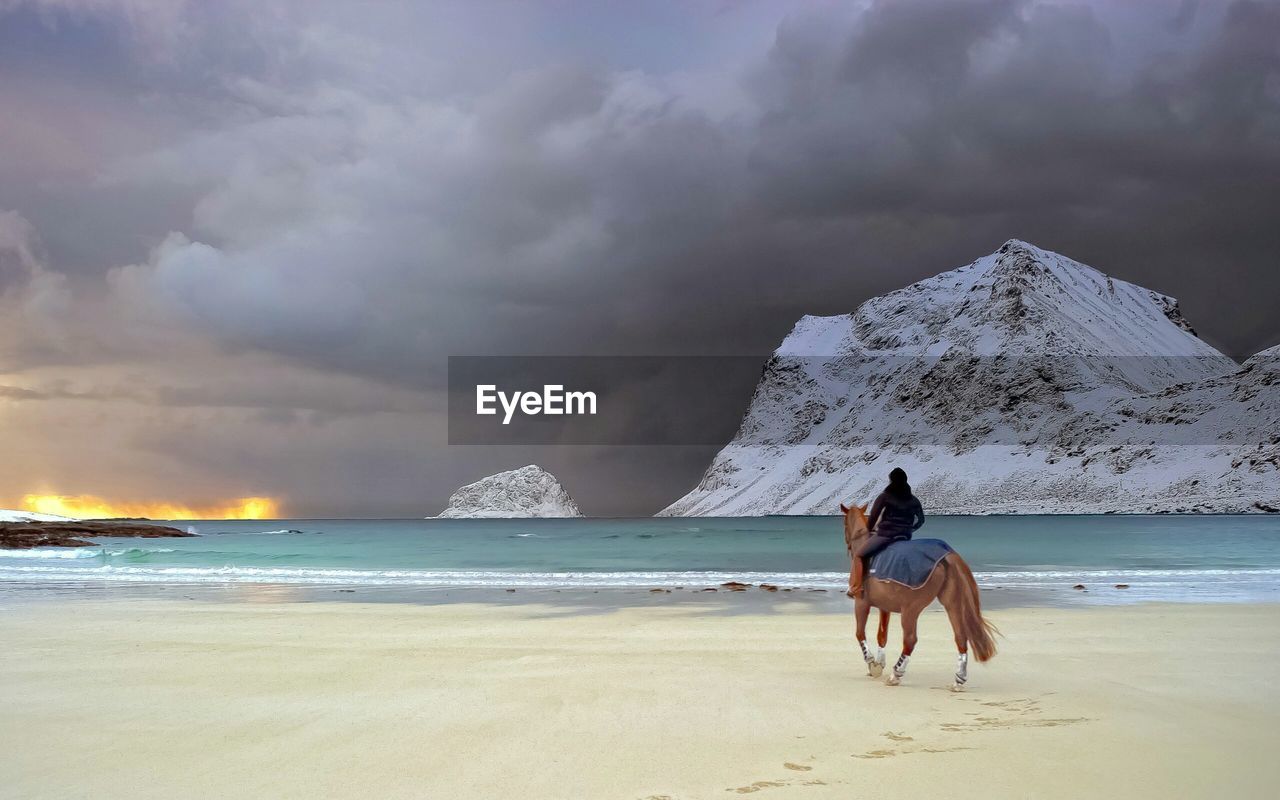 Man riding horse with sea and snow covered cliffs in background