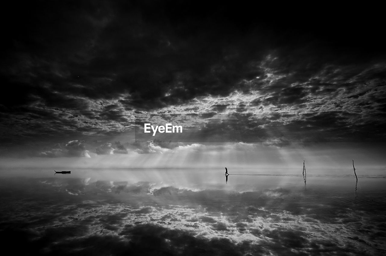 SILHOUETTE MAN STANDING IN WATER AGAINST SKY