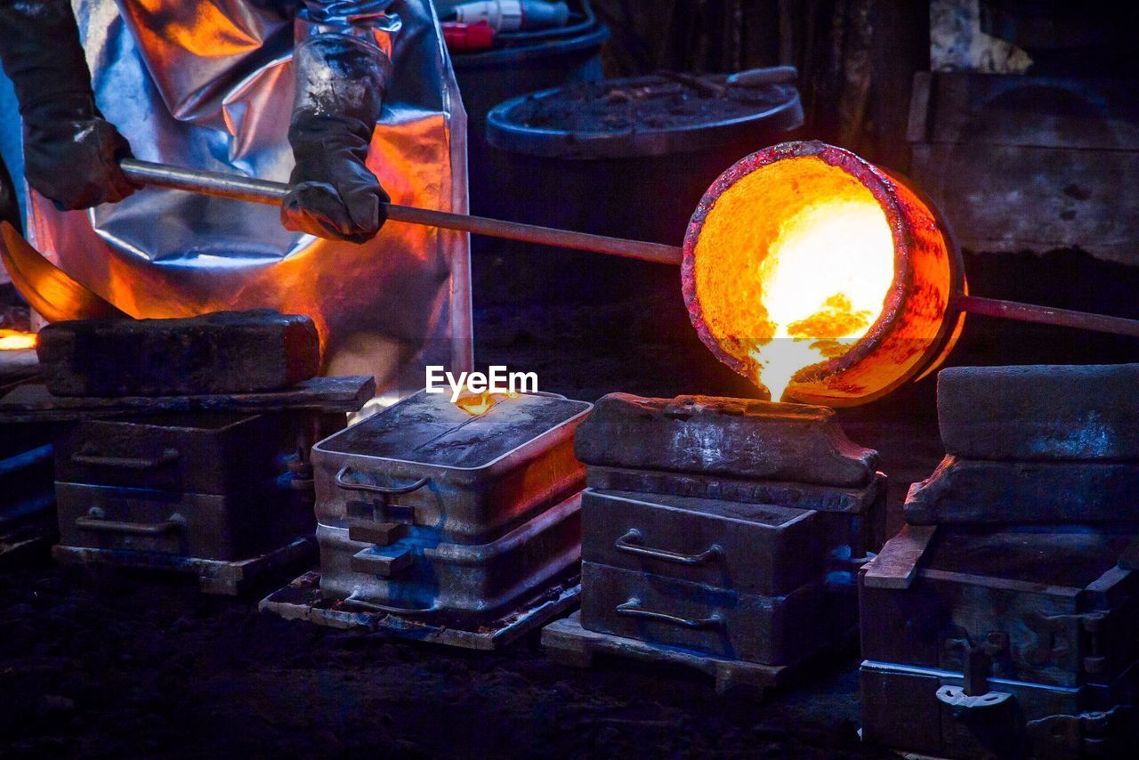 Midsection of worker pouring cast iron in container at still mill