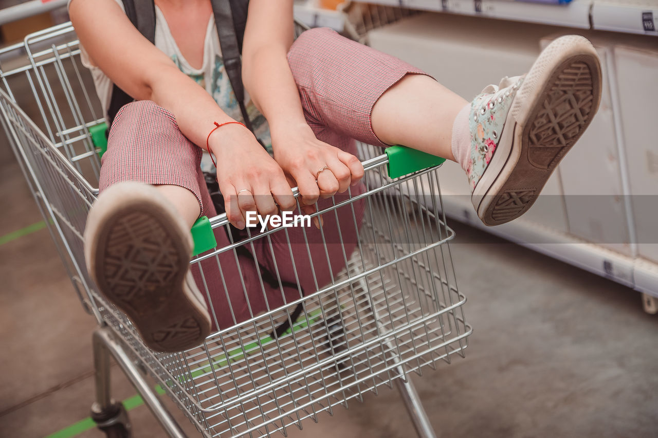 The lady's legs stick out of the basket in the shopping hall of the supermarket. riding in a cart