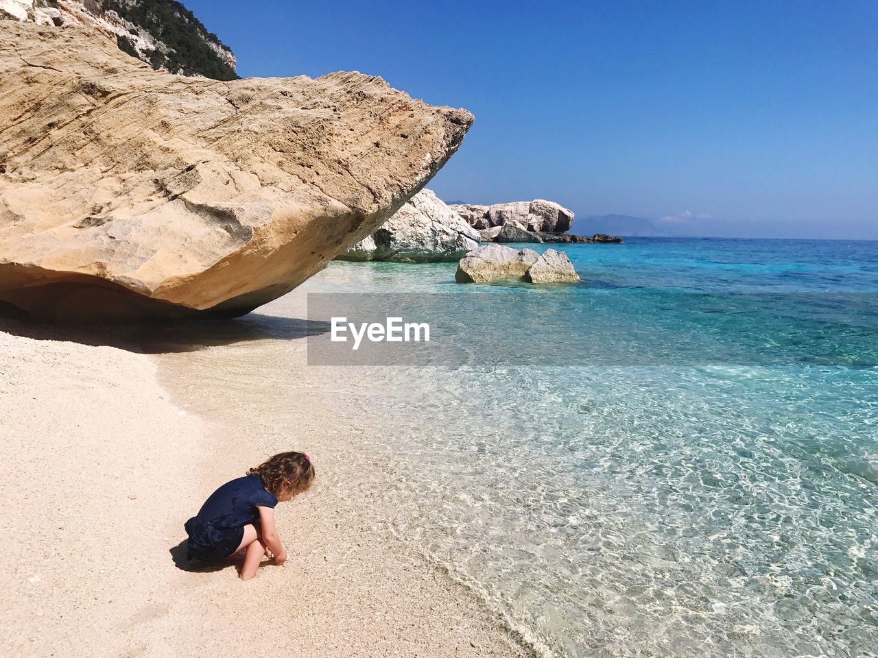 Child playing by rock by sea against clear sky