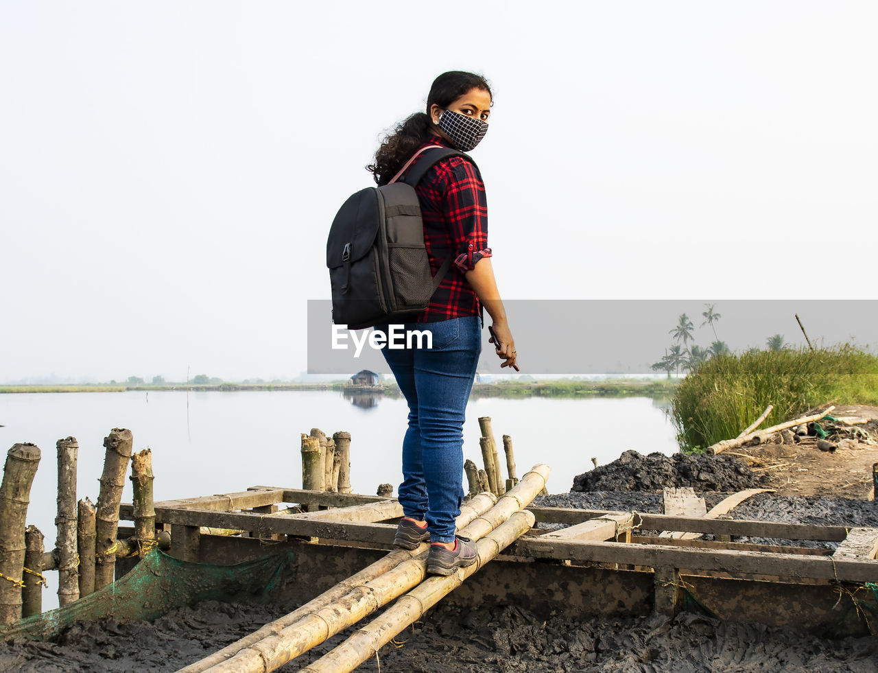 Full length of woman wearing mask standing against lake