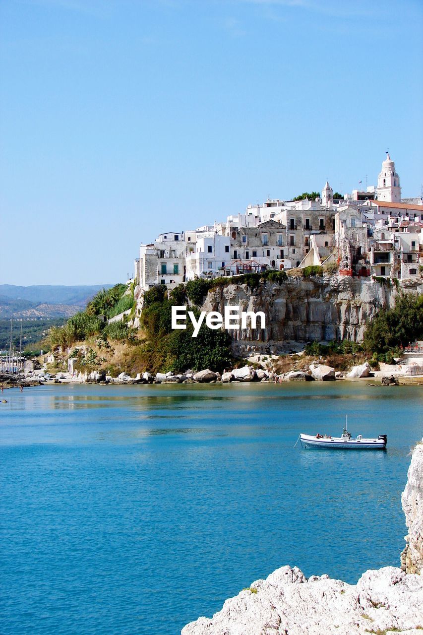 Buildings on cliff by sea against clear sky