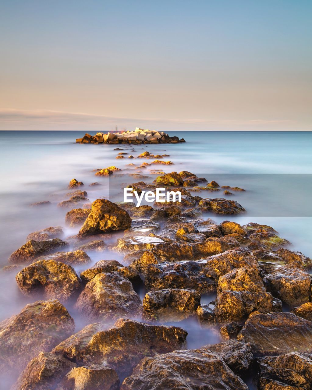 Rocks at seashore against sky during sunset